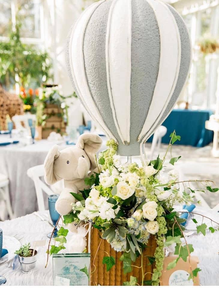 Gray and white hot air balloon centerpiece with a plush elephant over white roses and trailing greenery