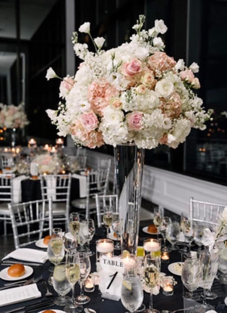 Tall pink and white centerpiece in a glass trumpet vase on a black-linen table at night