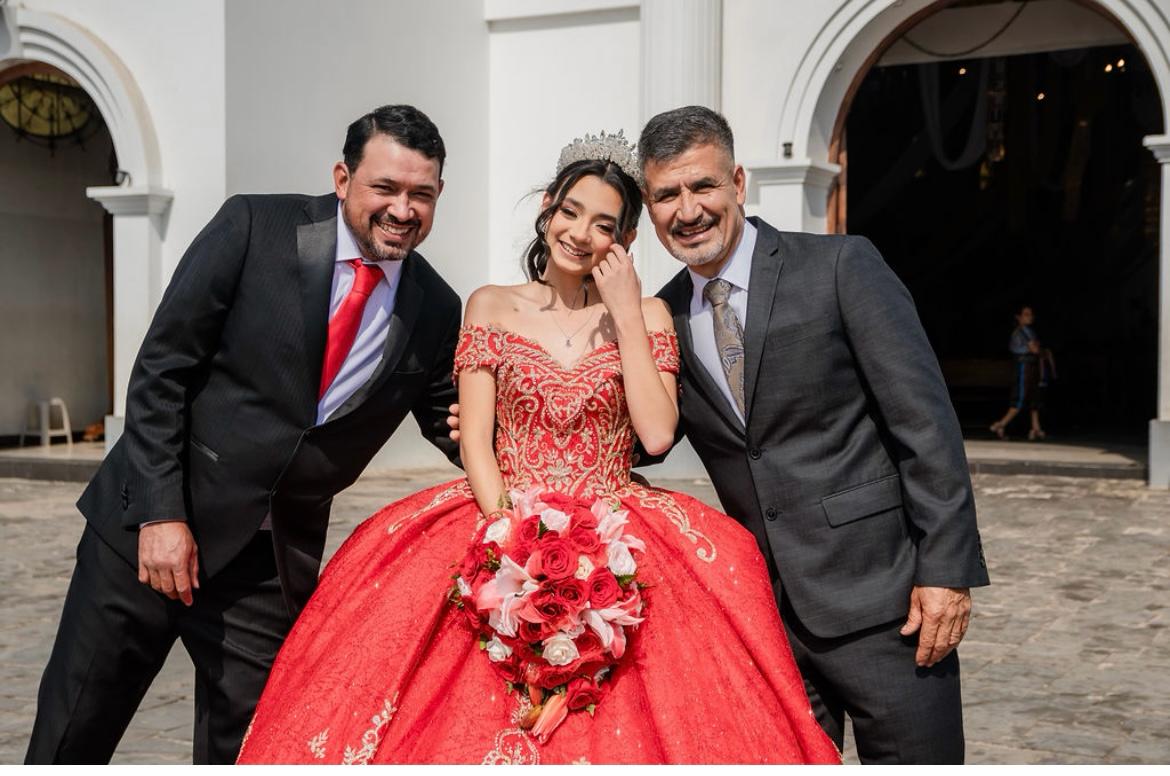 Quinceañera in a red gown with her bouquet between her father and grandfather outside the church