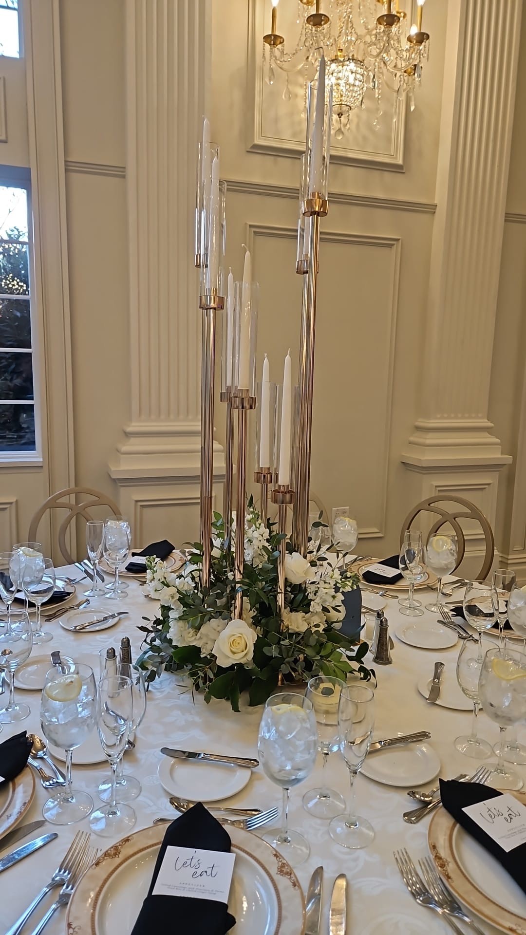 Gold candelabra centerpiece with white roses, stock and eucalyptus on a black-and-ivory place setting
