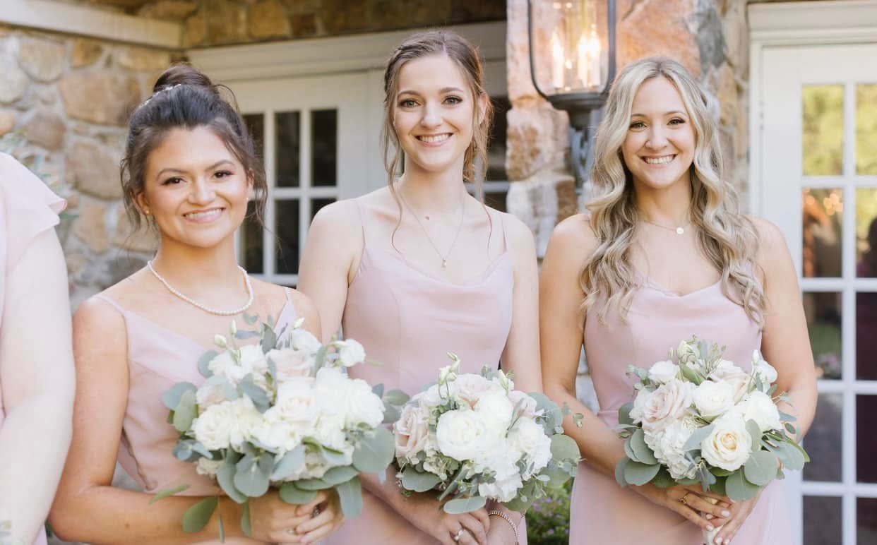 Bridesmaids in blush gowns holding white and blush bouquets with eucalyptus