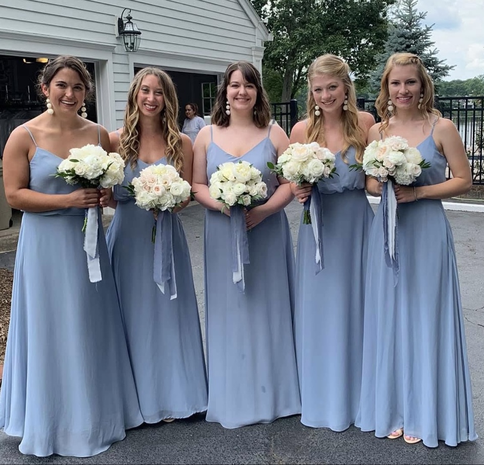 Bridesmaids in dusty blue gowns holding ivory rose bouquets tied with soft ribbon
