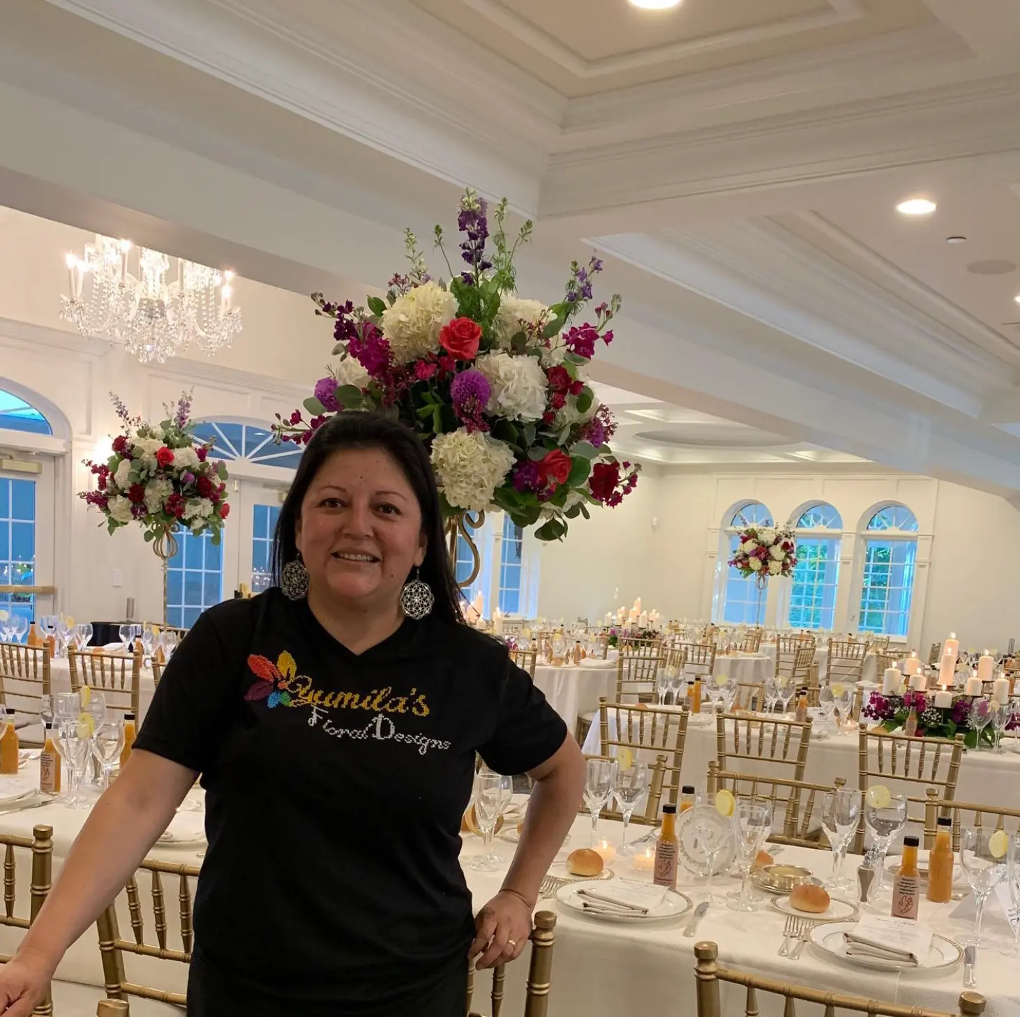 Yumila in a candlelit ballroom with tall jewel-tone centerpieces she designed for a New Jersey wedding