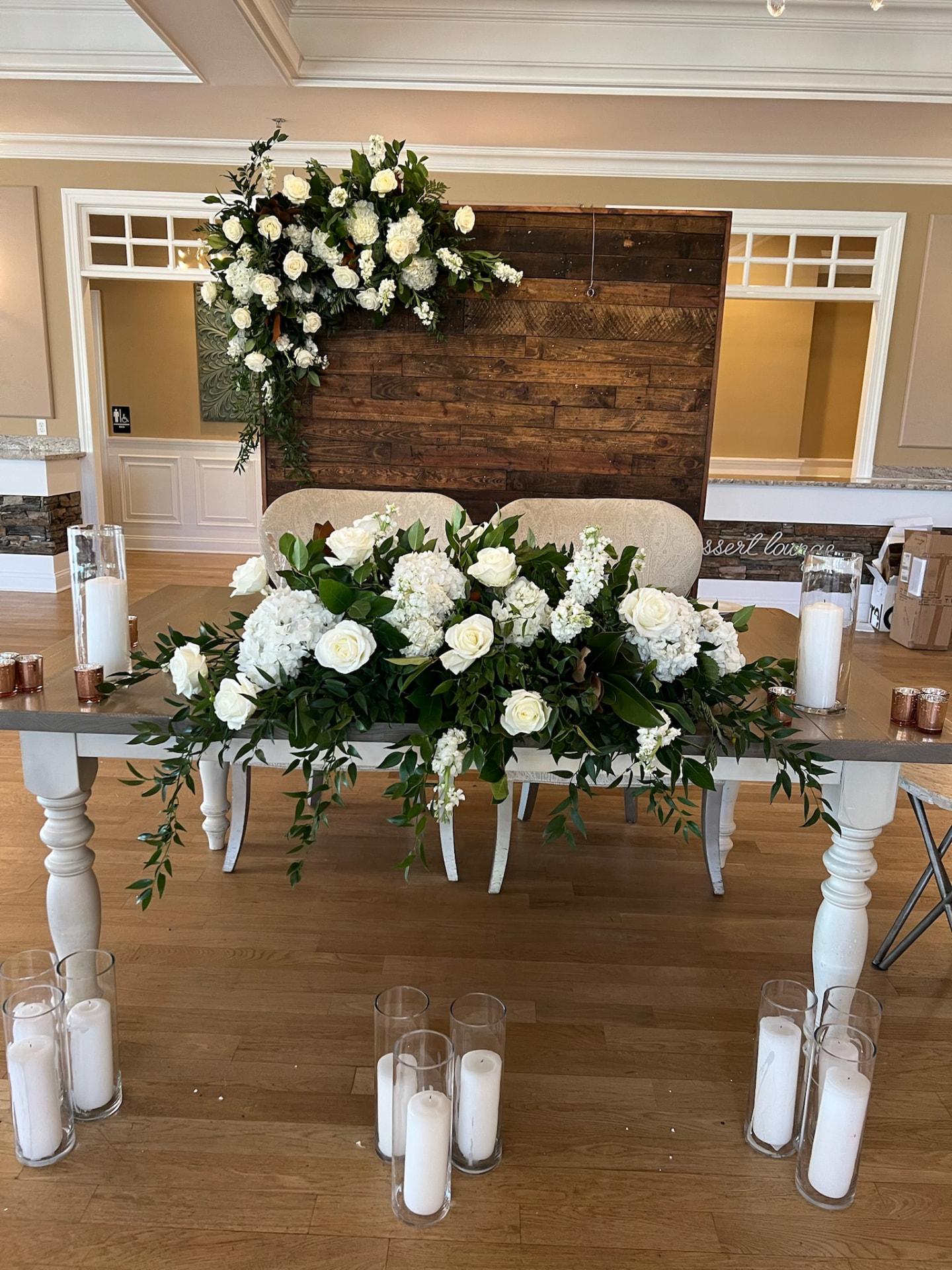 Farm-table sweetheart setting with a white rose and magnolia garland against a reclaimed wood backdrop