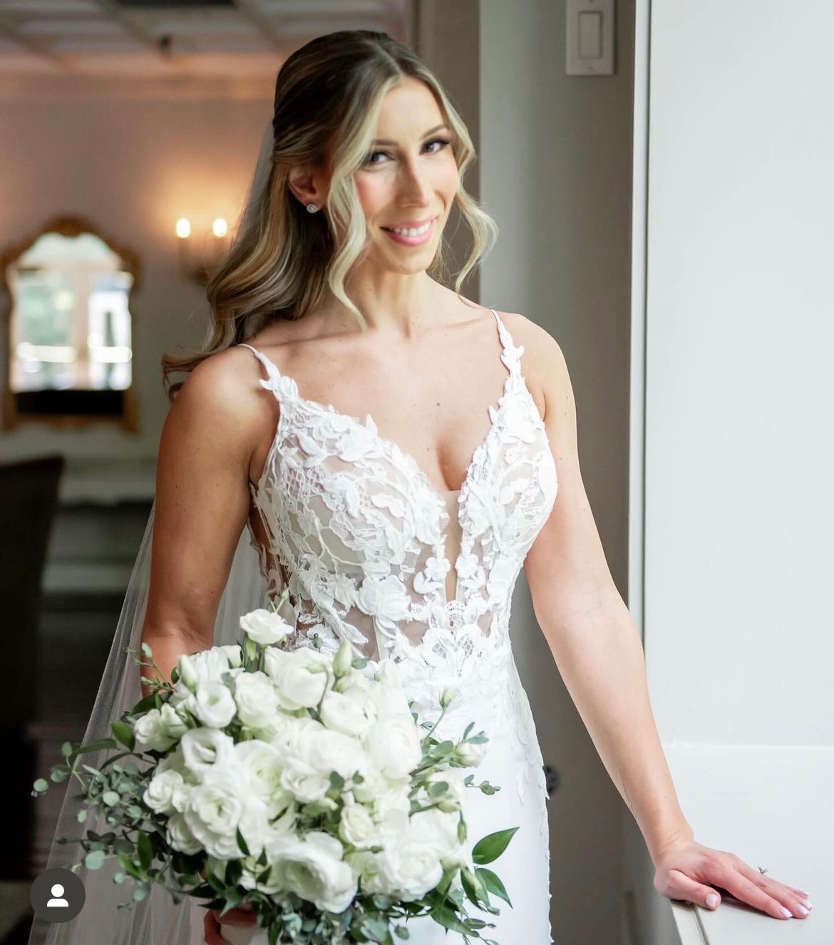 Bride holding a lush all-white bouquet of lisianthus, roses and ruscus greenery
