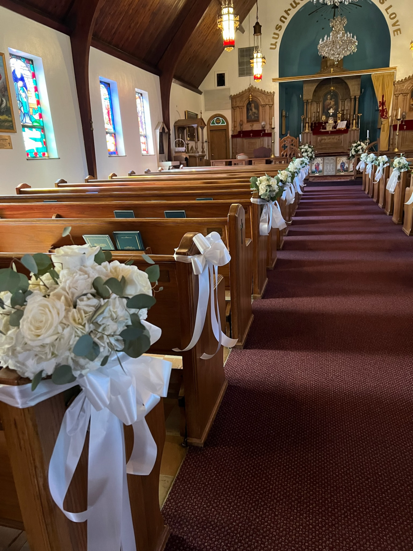 Church aisle lined with white rose and eucalyptus pew posies tied with satin ribbon