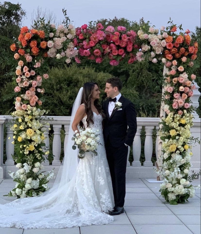 Bride and groom beneath a sunset ombre rose arch fading from coral to pink to ivory