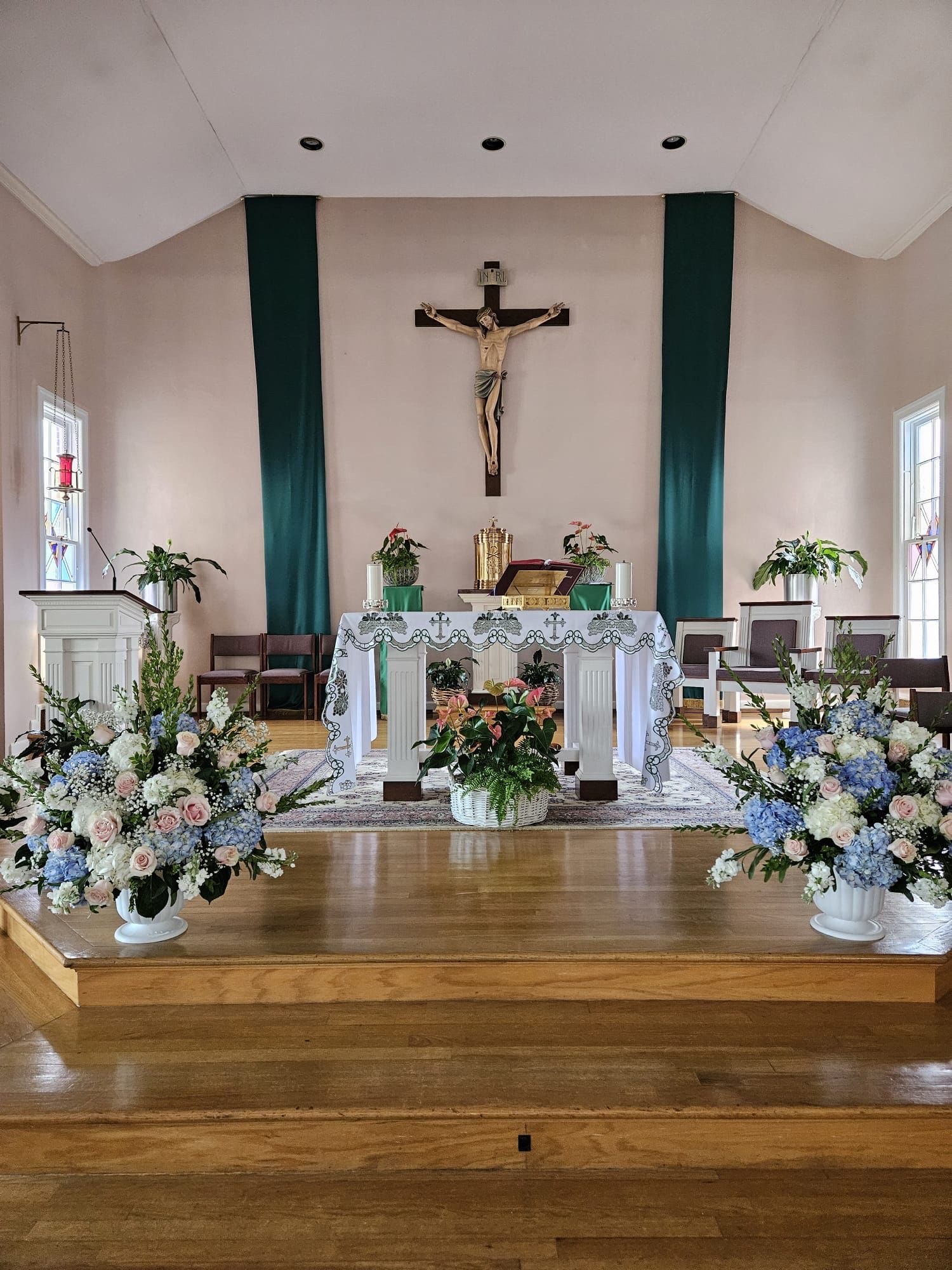 Church altar flanked by full arrangements of blue hydrangea, blush roses and white stock for a wedding ceremony