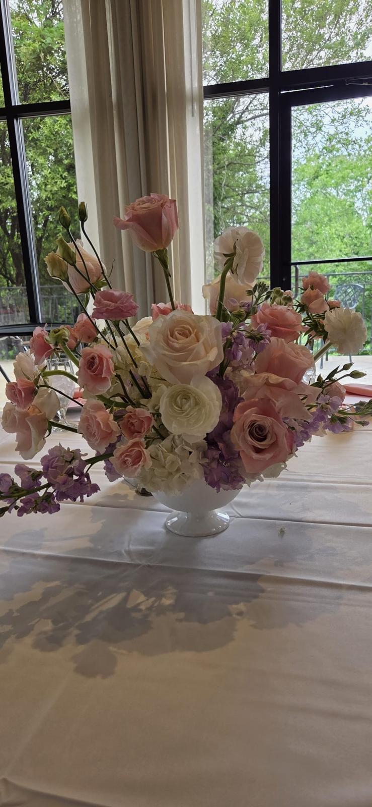 White footed compote of blush roses, lavender stock and ranunculus beside tall windows