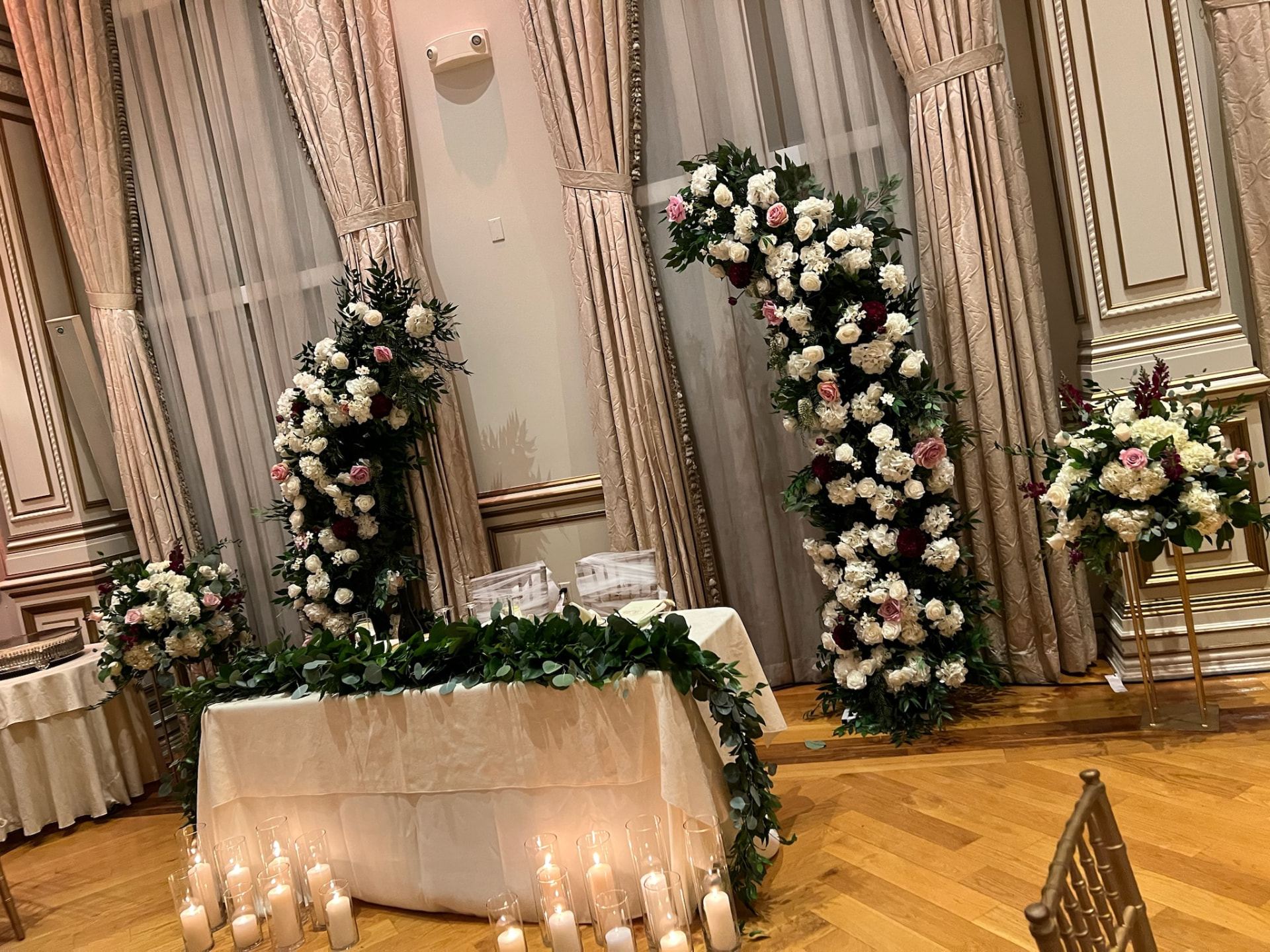 Sweetheart table with eucalyptus garland framed by asymmetric white, blush and burgundy floral columns
