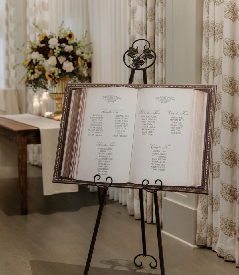 Seating chart styled as an open storybook on a black iron easel beside fall florals and candles