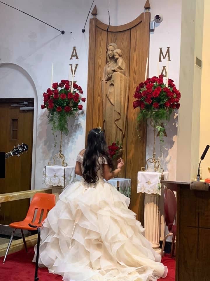 Tall red rose arrangements on gold pedestals flanking the altar of a church ceremony