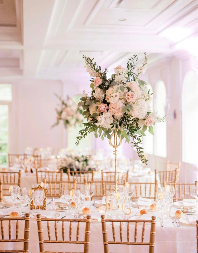 Tall blush and white centerpiece on a gold stand in a ballroom with gold chiavari chairs