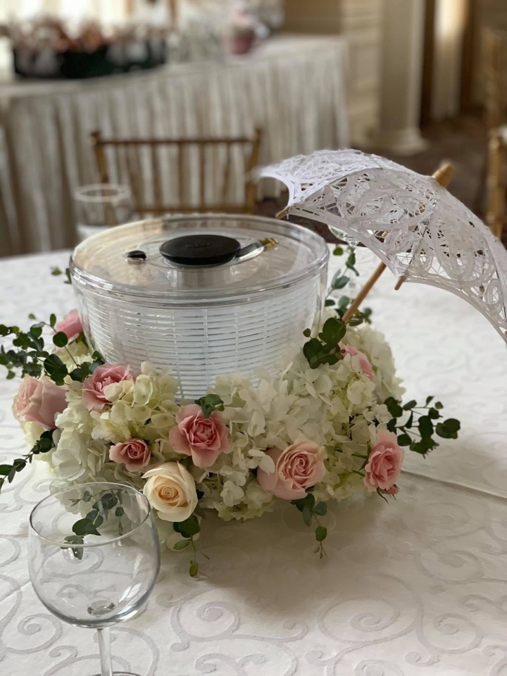 Clear acrylic bowl ringed with blush roses and white hydrangea topped with a lace parasol