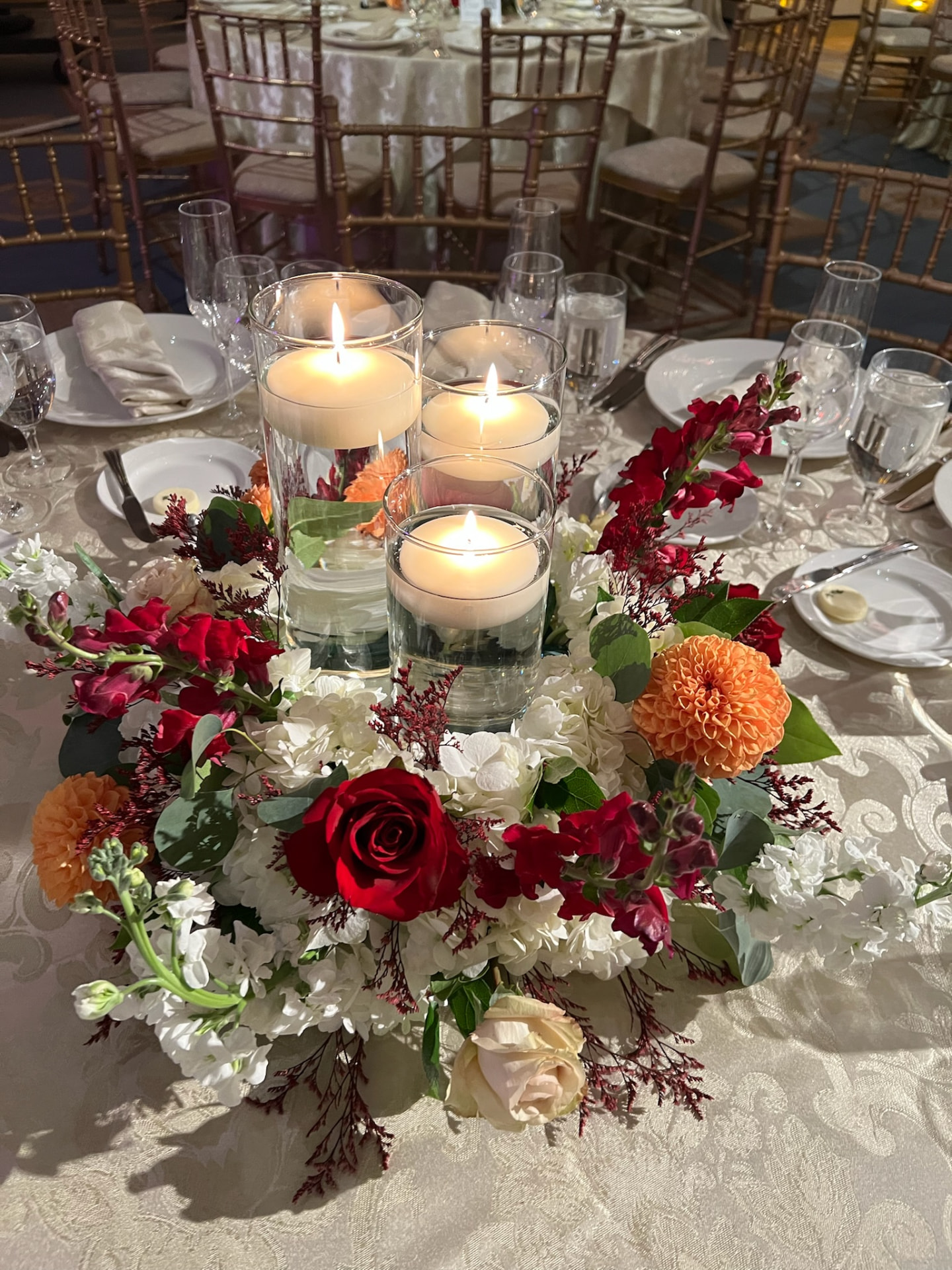 Low autumn centerpiece of red roses, orange dahlias and white hydrangea around floating pillar candles