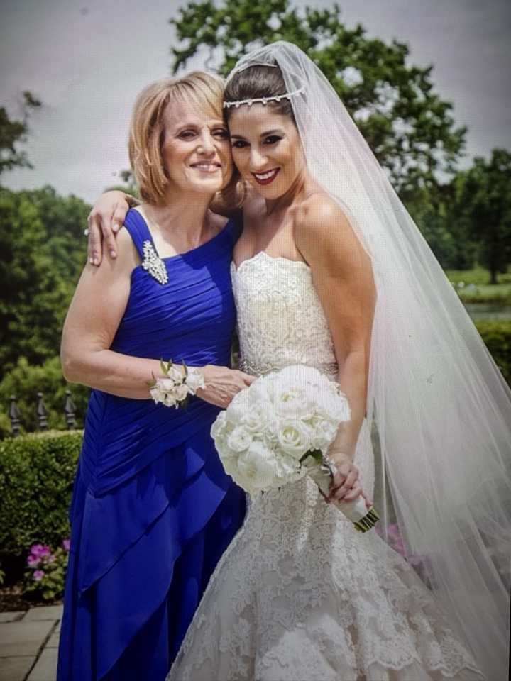 Bride holding a white rose bouquet beside her mother, who wears a matching white rose wrist corsage