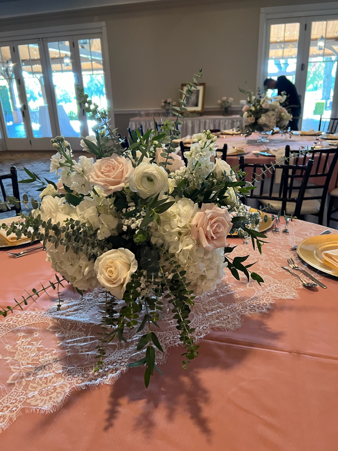 Low centerpiece of blush roses, white ranunculus, hydrangea and trailing eucalyptus on a coral and lace linen