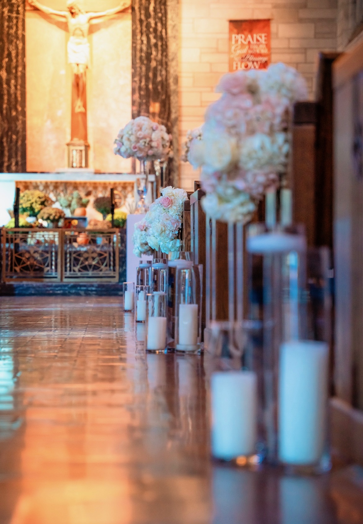 Blush and ivory pew arrangements with rows of pillar candles along a glowing church aisle