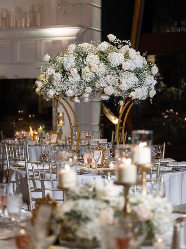 White hydrangea and rose arrangement atop a gold ring stand above a candlelit reception table