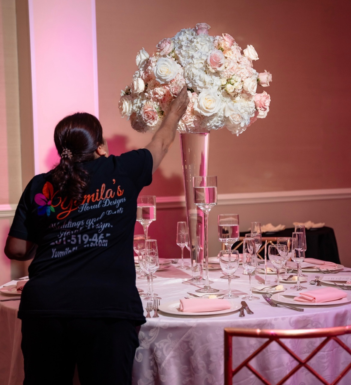 Yumila in a branded shirt placing a tall blush and ivory centerpiece before guests arrive