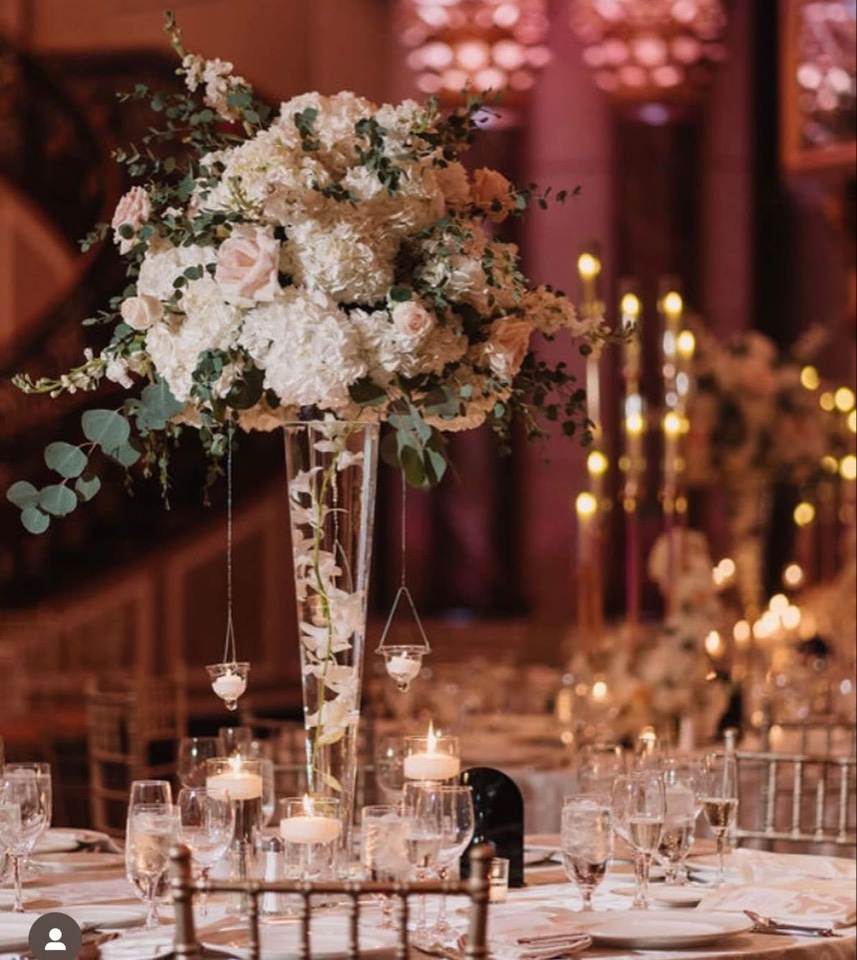 Tall trumpet vase centerpiece of white hydrangea and blush roses with hanging candles