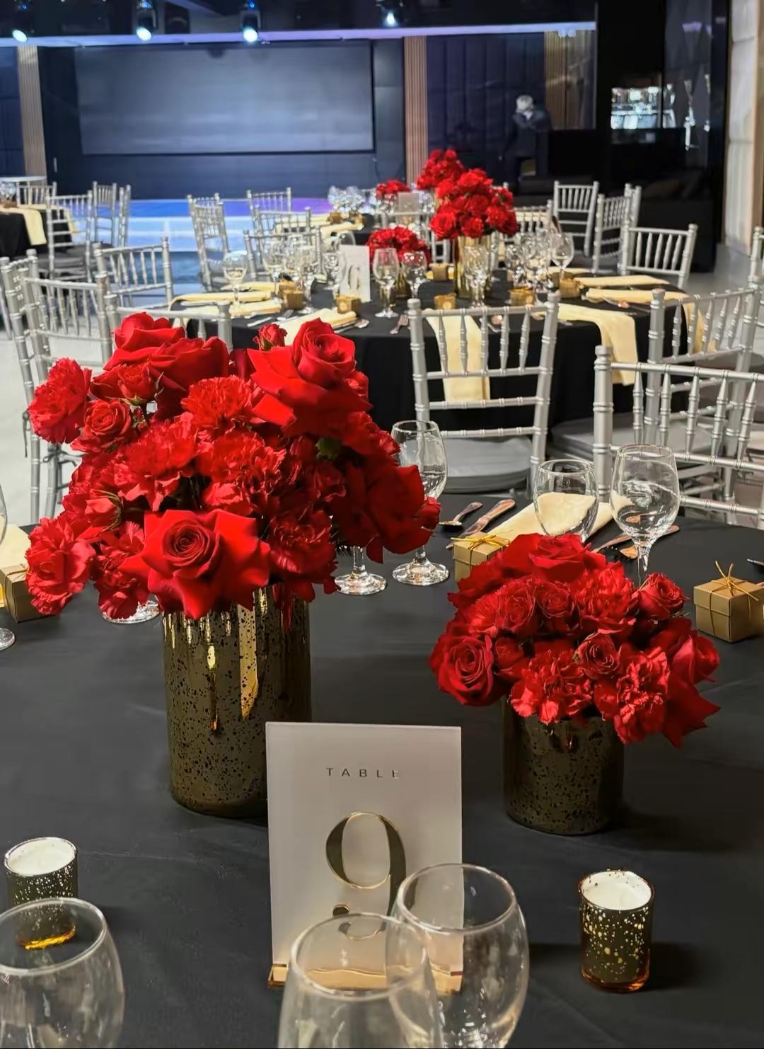 Gold mercury vases overflowing with red carnations and roses on a black table with a Table 9 marker