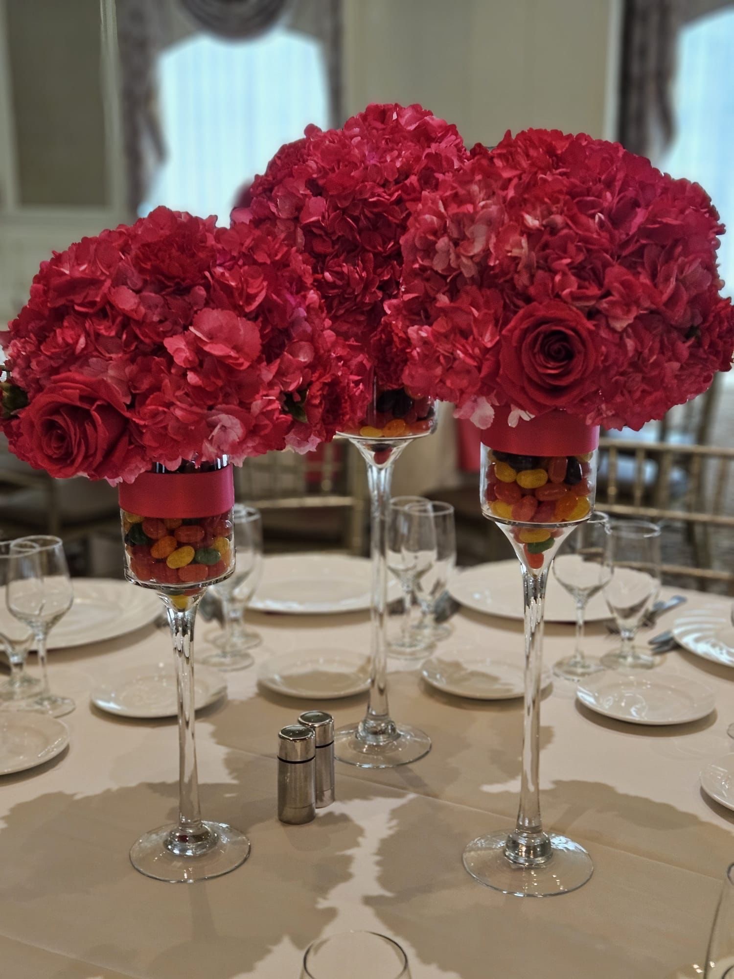 Elevated fuchsia hydrangea and rose centerpieces on glass stems filled with candy for a Sweet 16 celebration