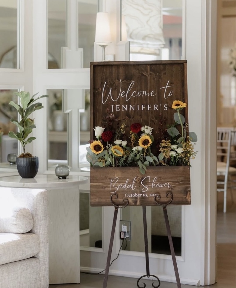 Wooden welcome sign for Jennifer's bridal shower with a planter of sunflowers and fall blooms
