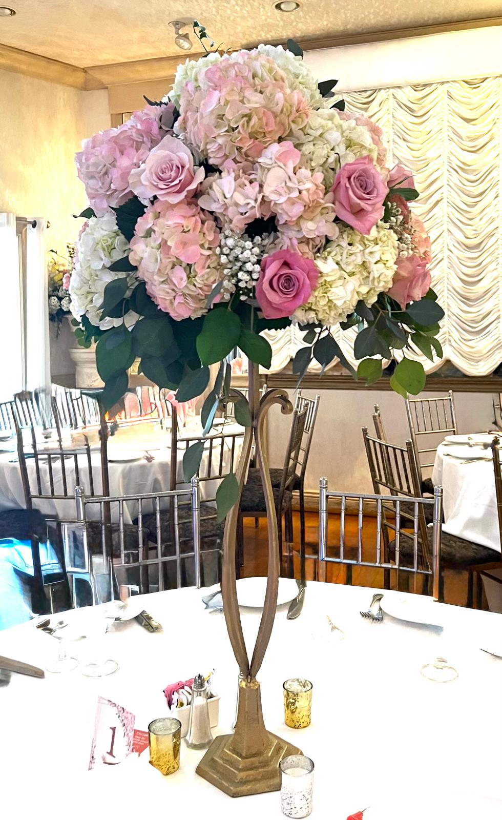 Tall gold stand overflowing with pink and white hydrangea, roses and eucalyptus above a banquet table