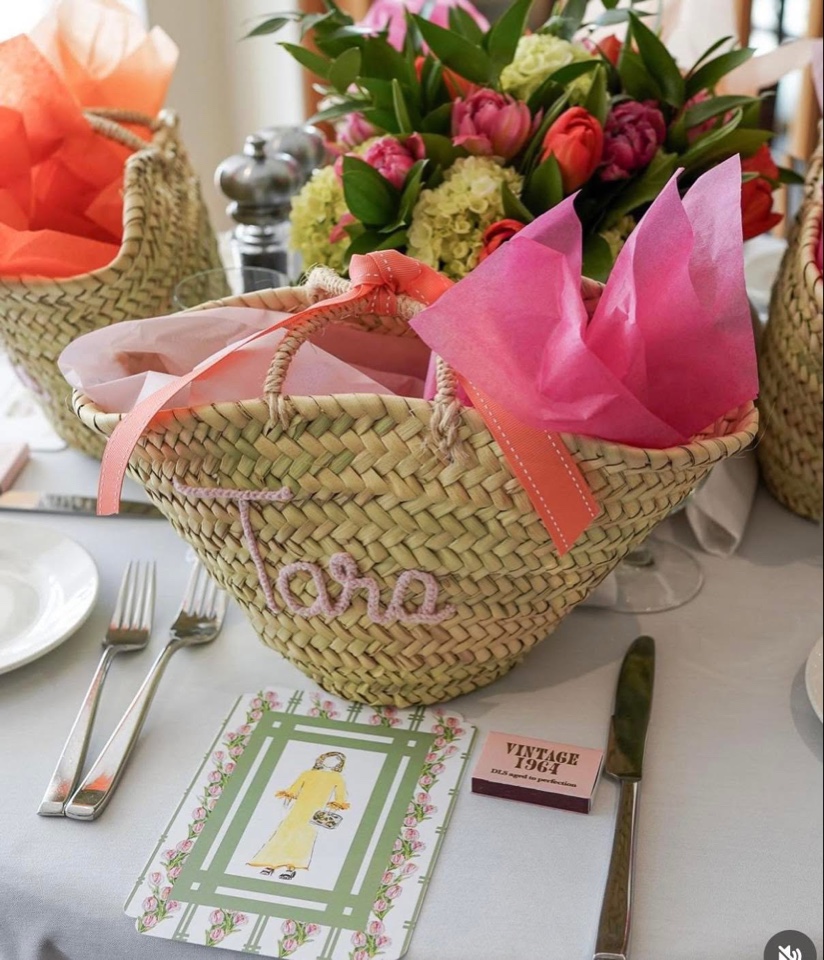 Straw guest tote embroidered Tara filled with pink tissue beside tulip centerpieces