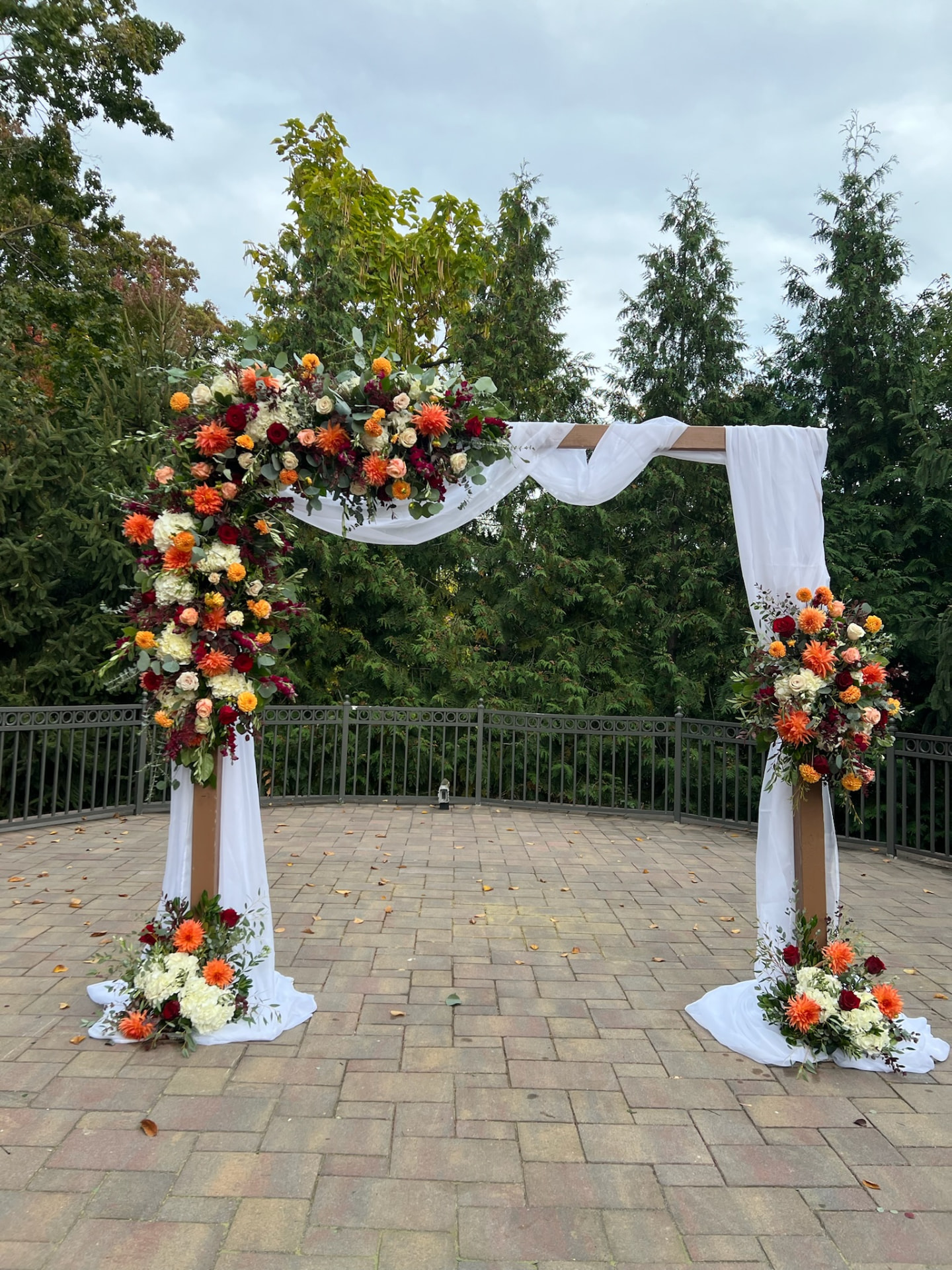 Draped outdoor wedding arch with orange dahlias, burgundy roses and cream hydrangea on a terrace
