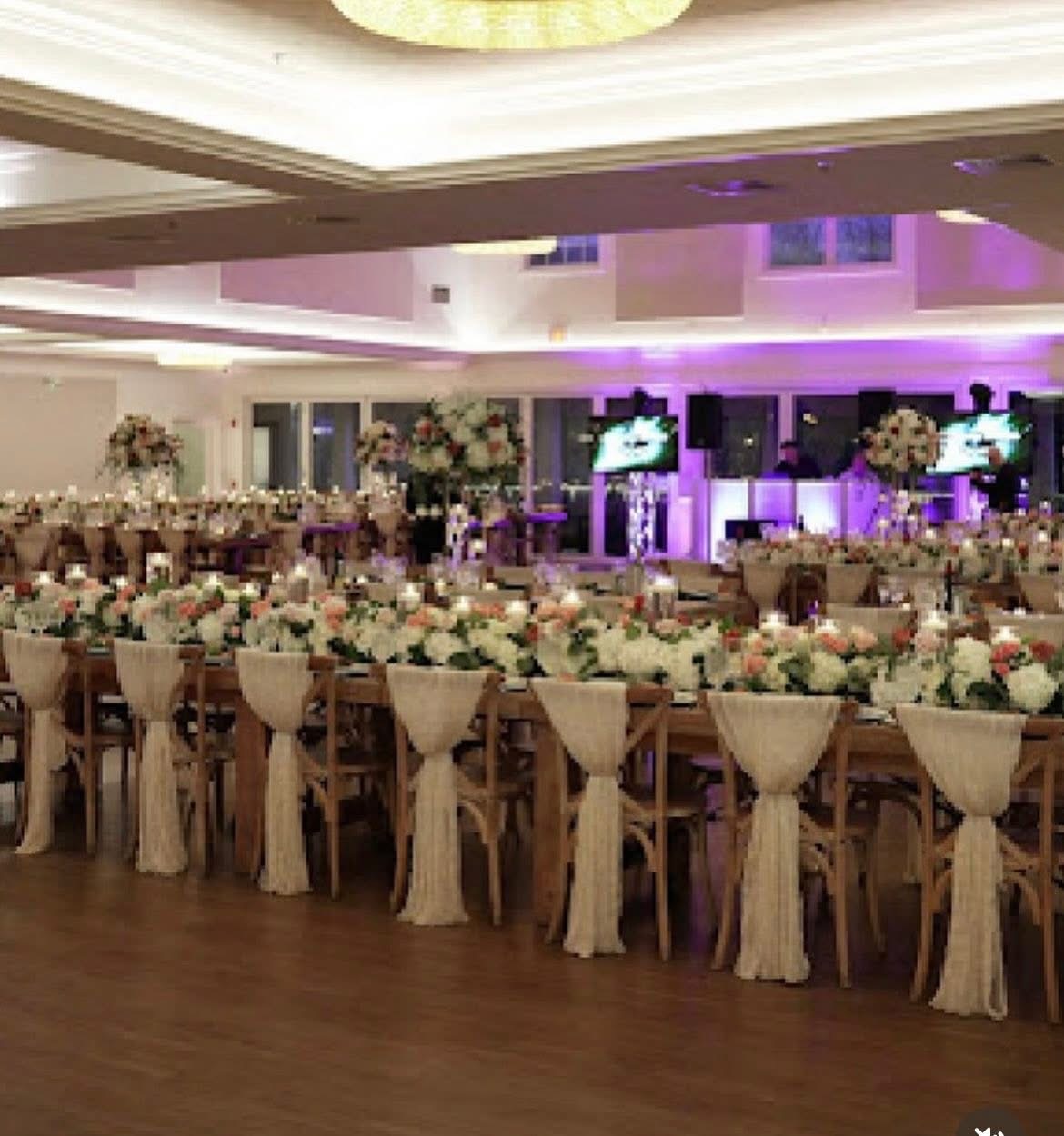 Ballroom reception with farm tables, ivory chair sashes, and blush and white centerpieces