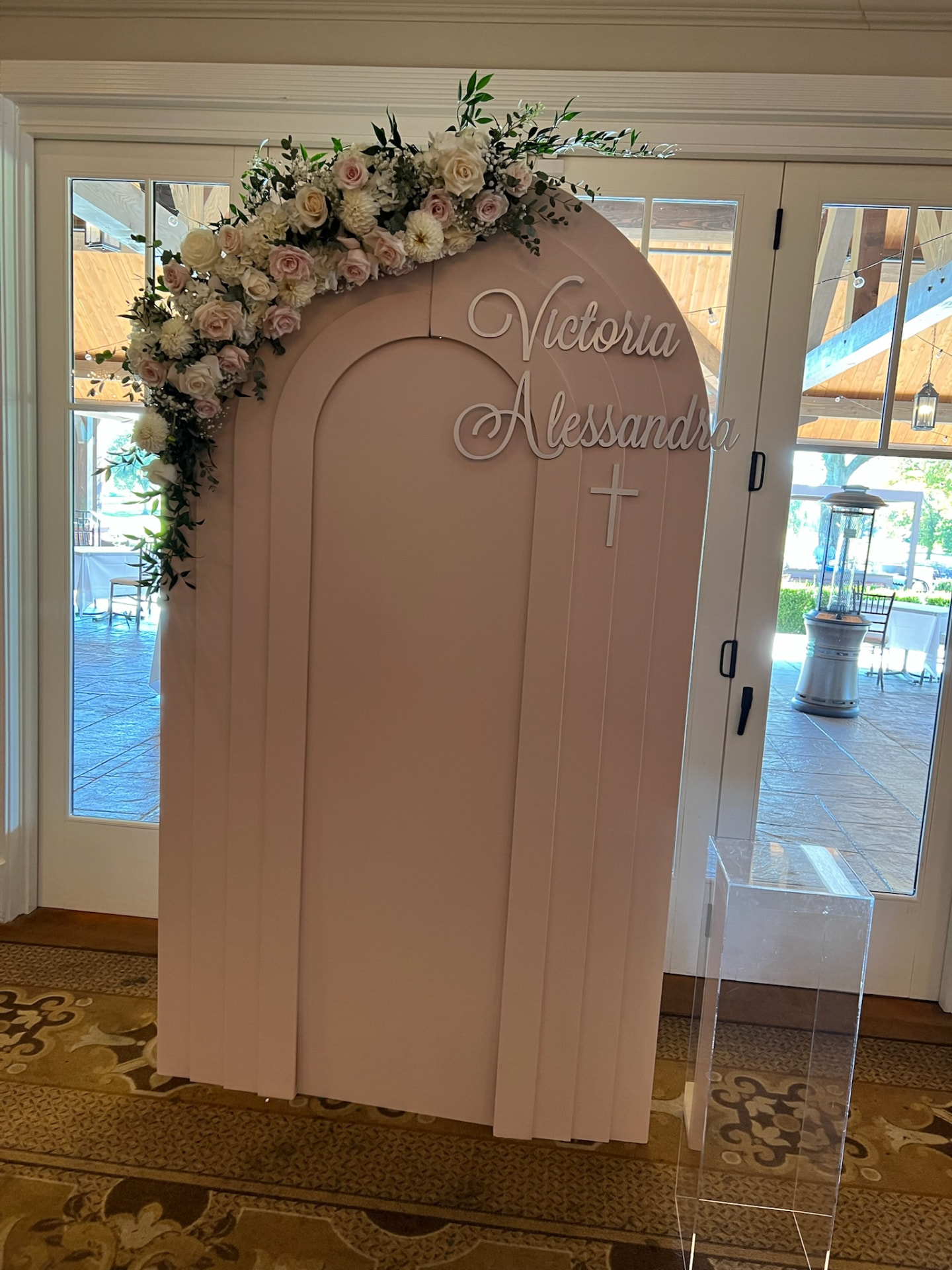 Blush arched welcome backdrop crowned with cream roses, dahlias and greenery for a family celebration