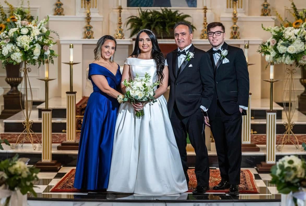 Bride with her family at the church altar holding an all-white bouquet of roses and stock with eucalyptus