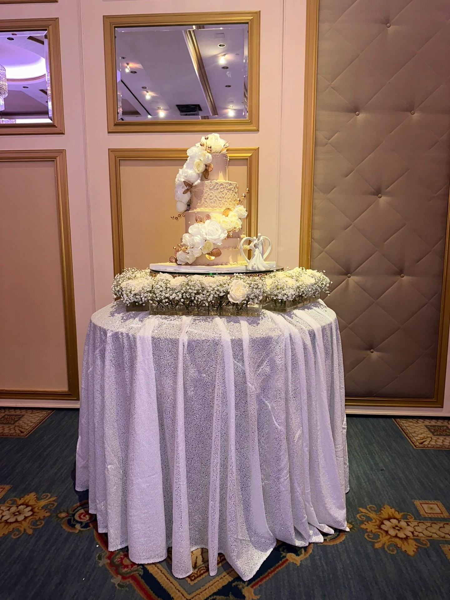 Wedding cake table ringed with baby’s breath and white roses in a candlelit ballroom