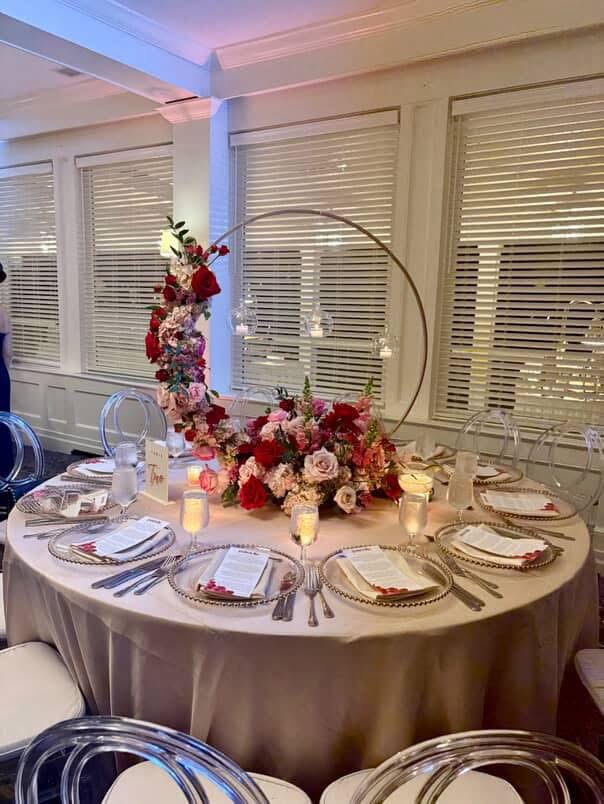 Gold hoop centerpiece of red and blush roses with hanging glass candle globes on a round reception table