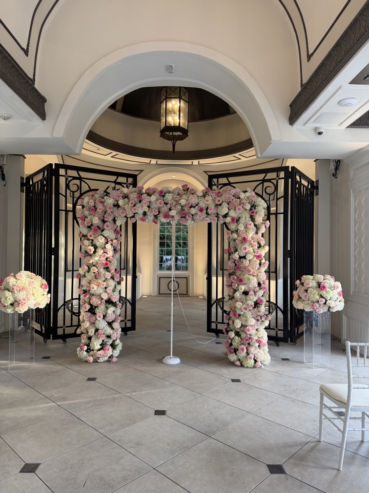 Blush and ivory rose arch framing wrought iron gates in a white ballroom rotunda