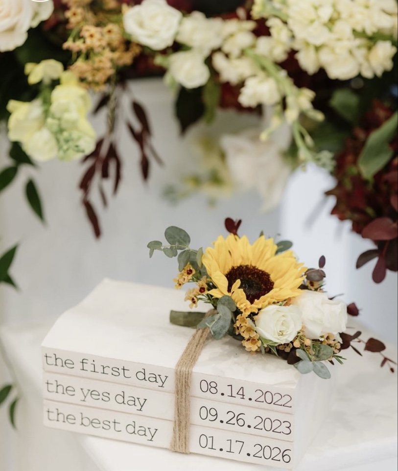 Sunflower and white rose boutonniere resting on a stack of books marking the first day, yes day and best day