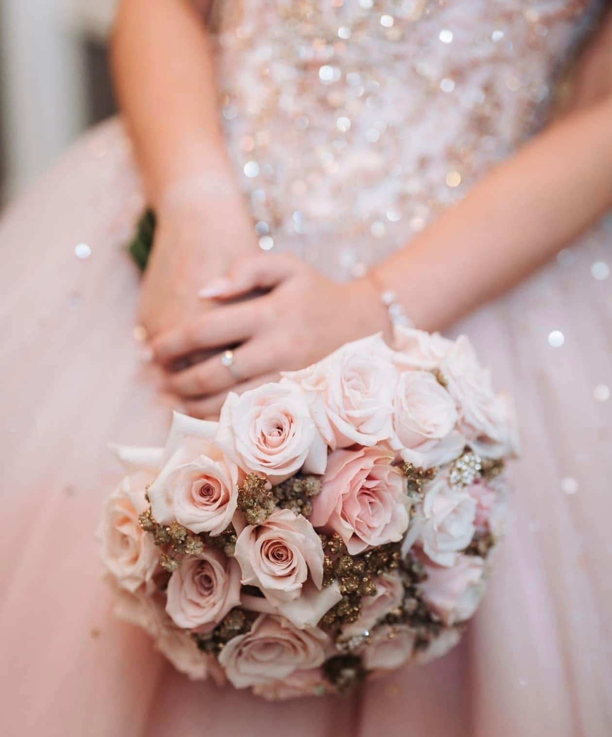 Birthday girl in a sparkling blush gown holding a bouquet of blush roses with gilded baby's breath