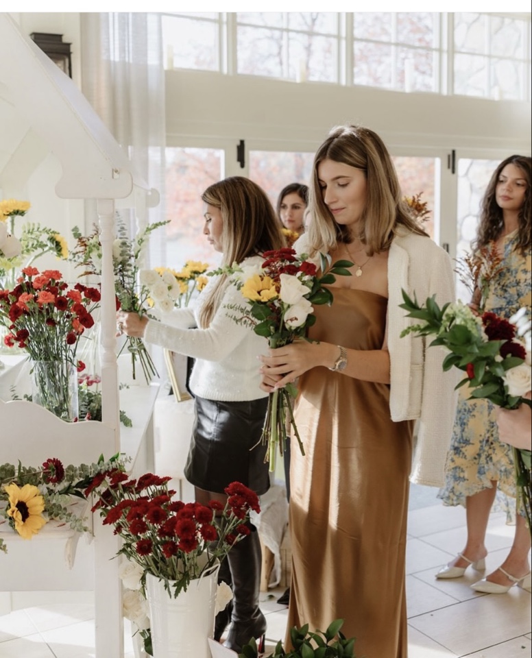 Guests arranging hand-tied bouquets of sunflowers, red carnations and white roses at a bloom bar