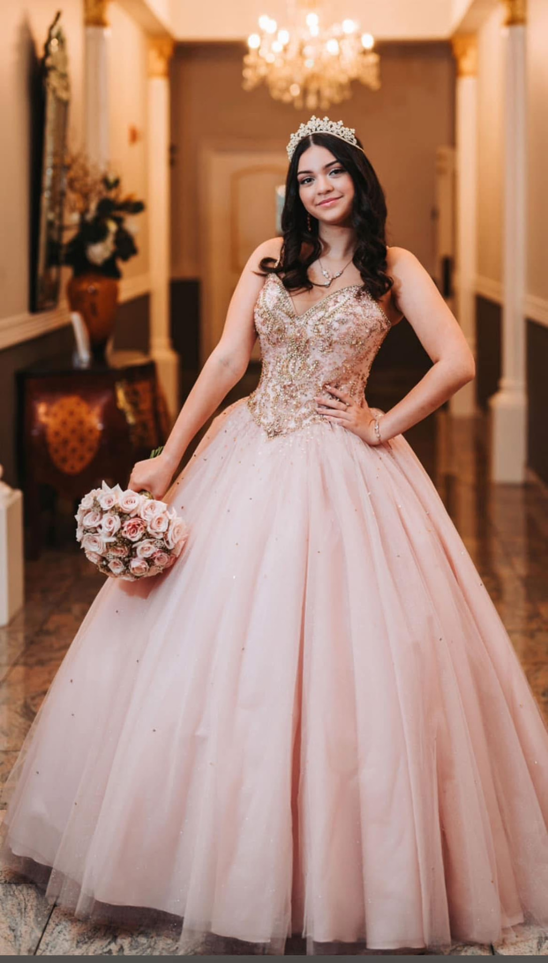 Quinceañera in a blush ball gown holding a hand-tied bouquet of blush roses and gilded accents