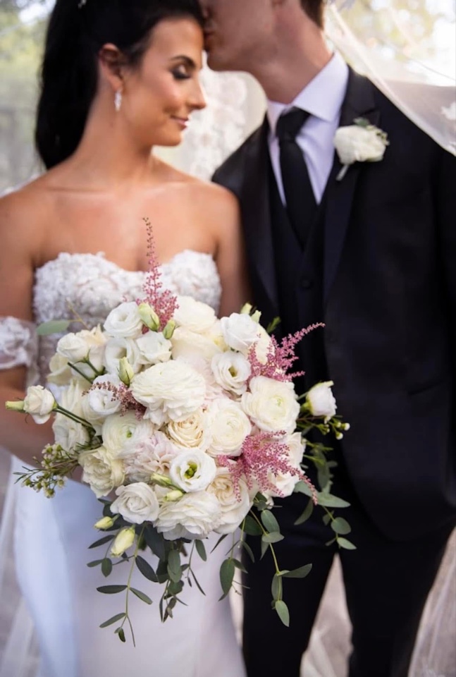 Bridal bouquet of white ranunculus, lisianthus and pink astilbe with a matching white rose boutonniere