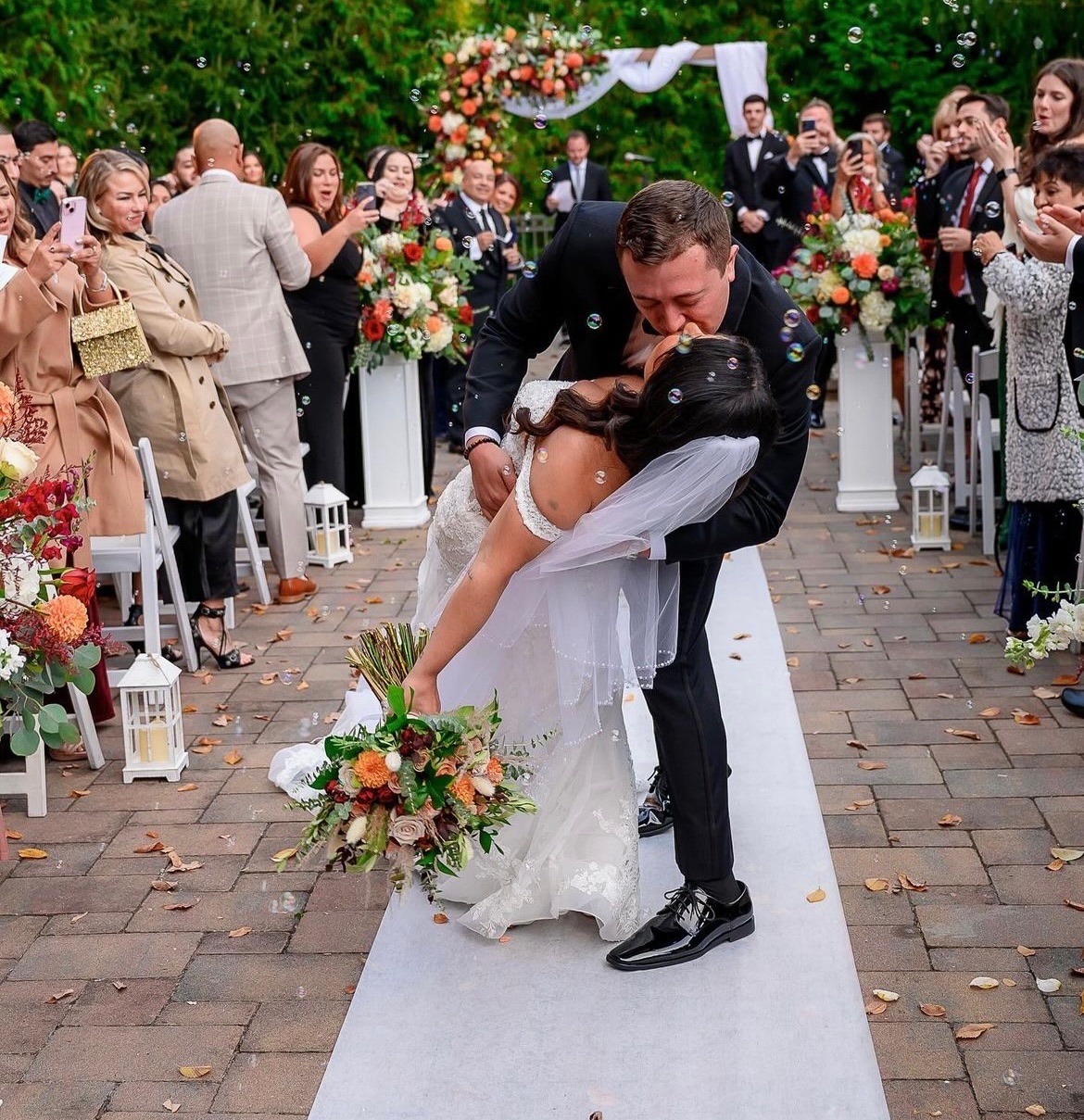 Recessional kiss down a stone aisle lined with autumn pedestal florals, lanterns and bubbles