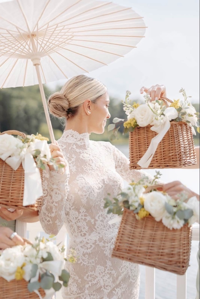 Bride with a parasol beside wicker baskets filled with white and yellow blooms tied with ribbon
