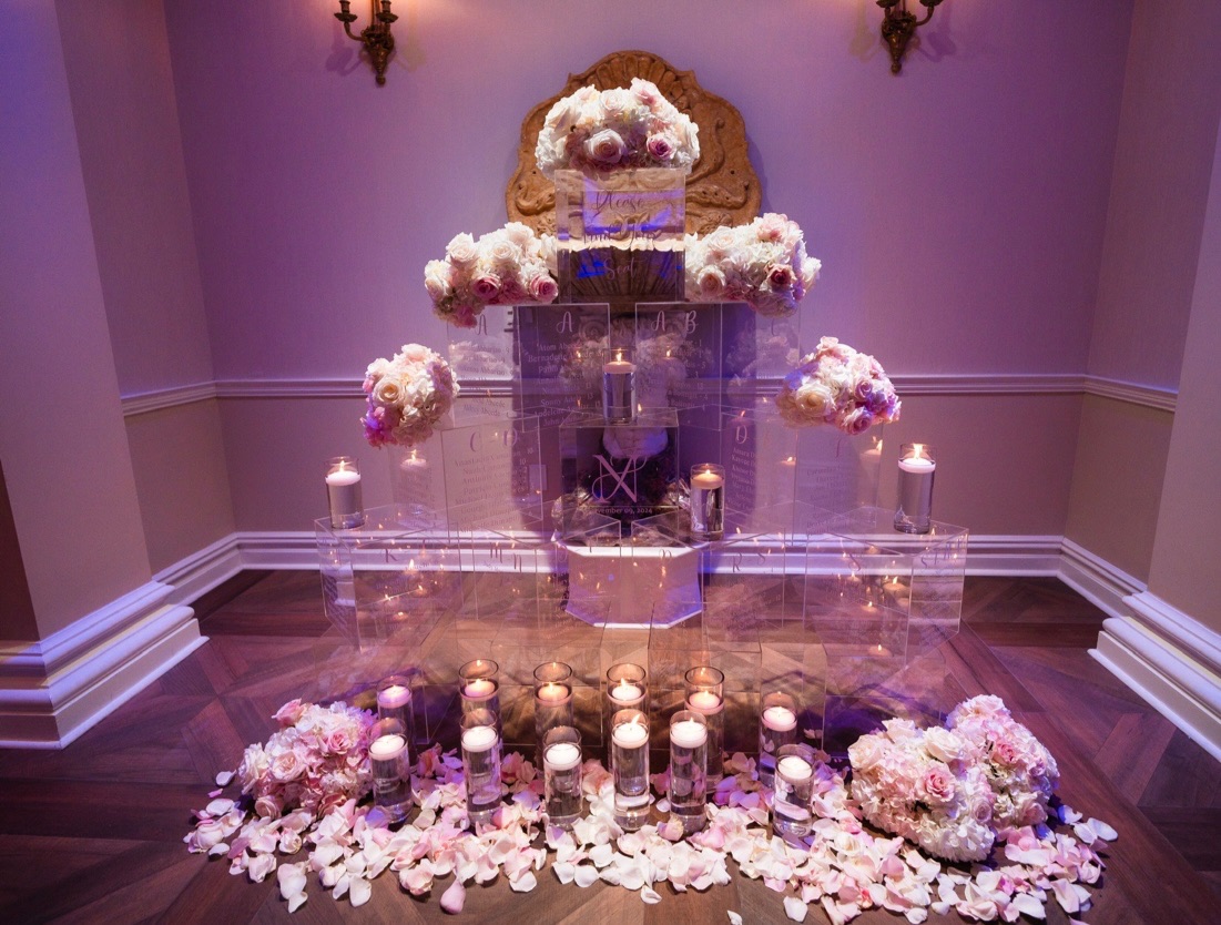 Tiered acrylic seating chart display with blush rose clusters, floating candles and rose petals