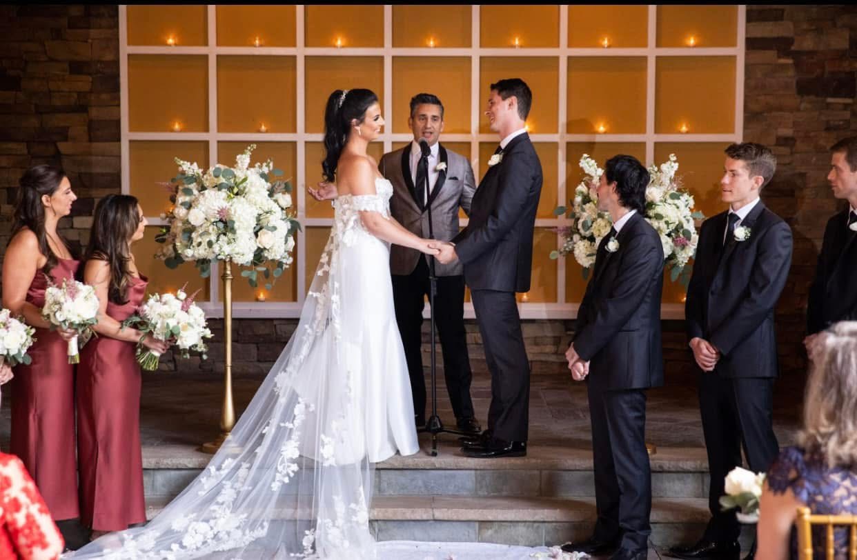 Couple exchanging vows between tall white and blush arrangements on gold pedestals