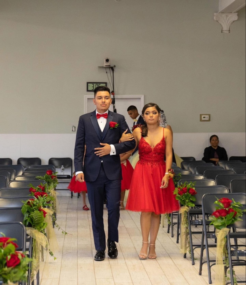 Court of honor walking down an aisle lined with red rose and greenery chair markers