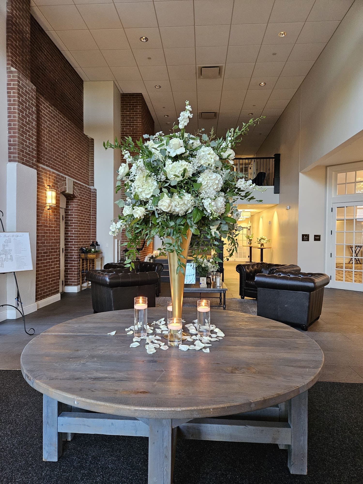 Tall gold trumpet vase of white hydrangea, roses and eucalyptus greeting guests in a venue entry lounge