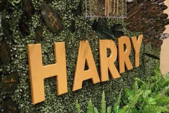Boxwood greenery seating wall with gold letters, ferns and hand-lettered magnolia leaf place cards