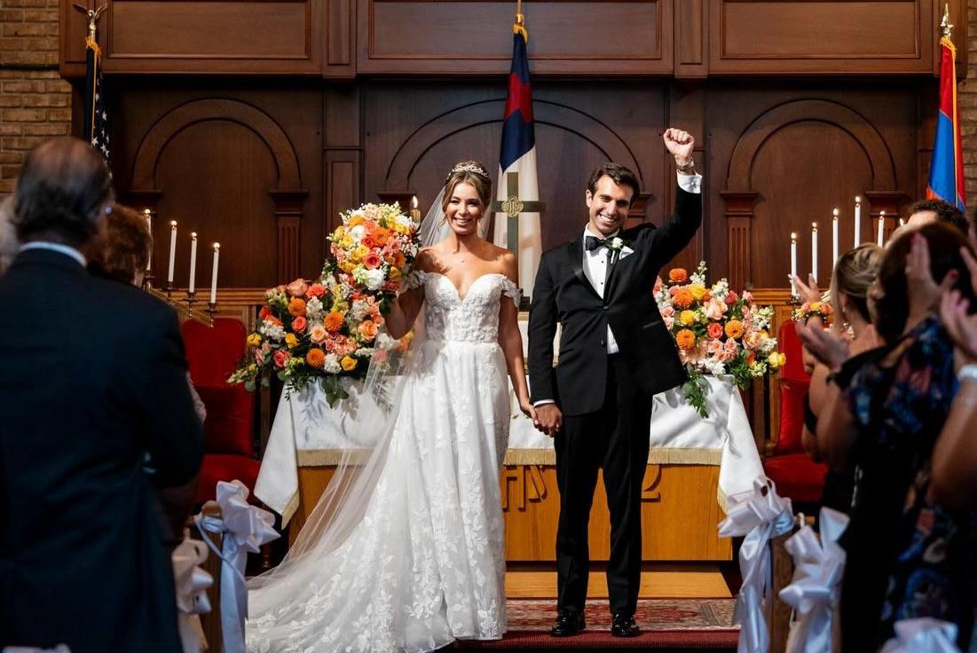 Church recessional with bright orange and coral arrangements lining the altar